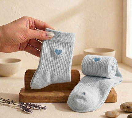 Gray baby socks with blue hearts held by a hand on a wooden stand.