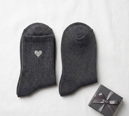 Pair of dark gray socks with a heart design next to a small gift box on a white background