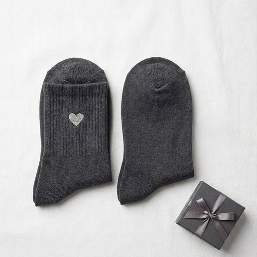 Pair of dark gray socks with a heart design next to a small gift box on a white background
