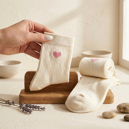 White baby socks with pink hearts held by a hand on a wooden stand.
