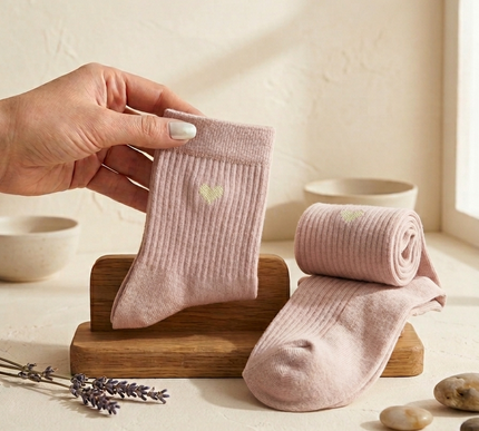 Person holding a pink sock with another sock rolled up on a wooden stand against a light background.