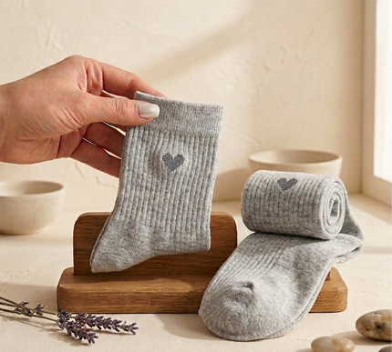 Gray baby socks with a heart design held by a hand on a wooden stand.