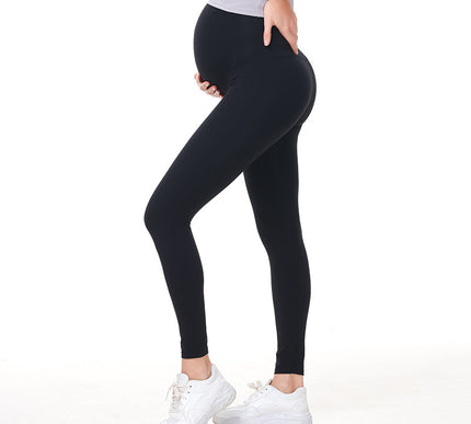 Pregnant Person wearing black leggings and white sneakers on a white background
